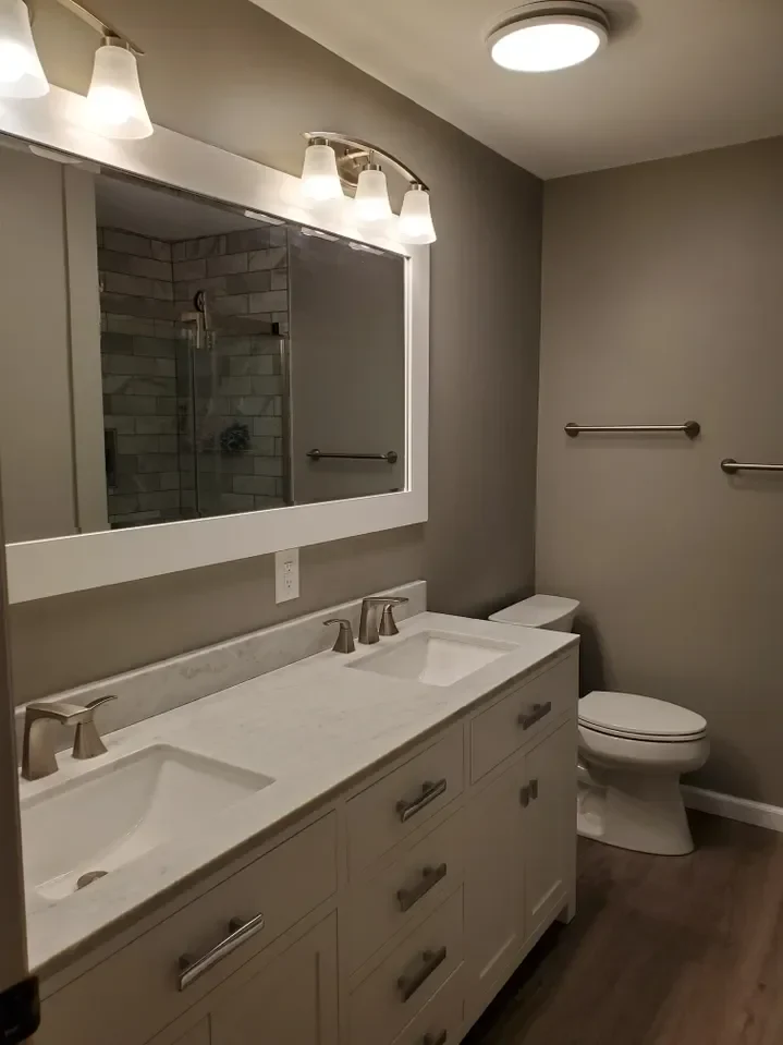 Modern bathroom with a double vanity, marble countertop, stylish light fixtures, and a walk-in shower in a neutral-colored space.