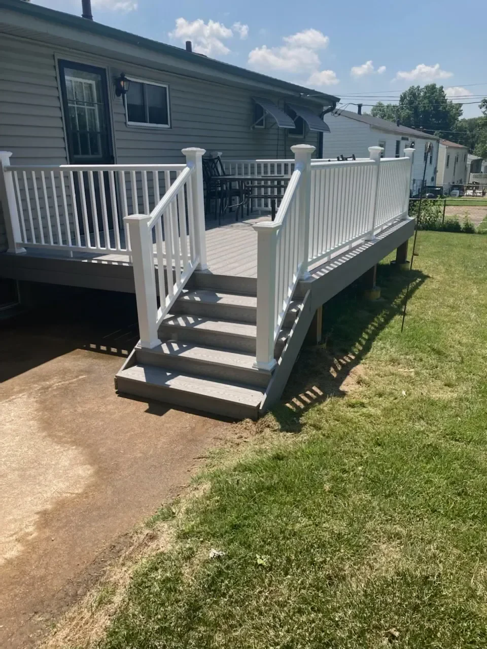 A modern white deck with stairs connects to a home, surrounded by green grass on a sunny day.