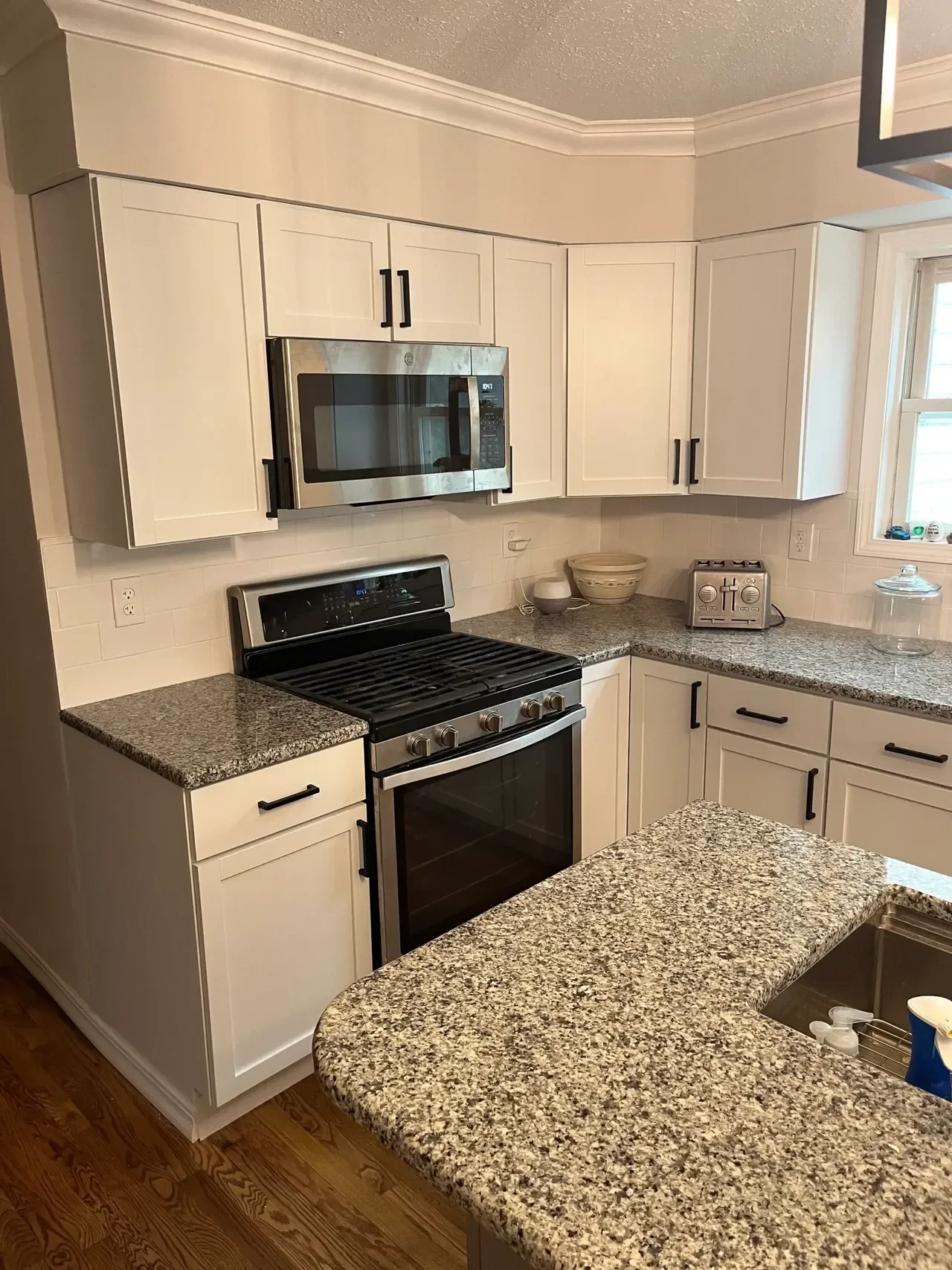 A modern kitchen with white cabinetry, granite countertops, a stainless steel oven, microwave, and wooden flooring. Bright and inviting space.