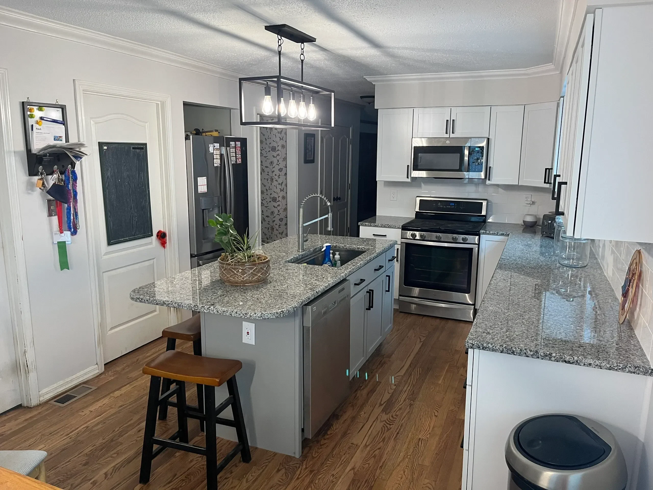 Modern kitchen featuring granite countertops, stainless steel appliances, a pendant light fixture, and wooden bar stools.